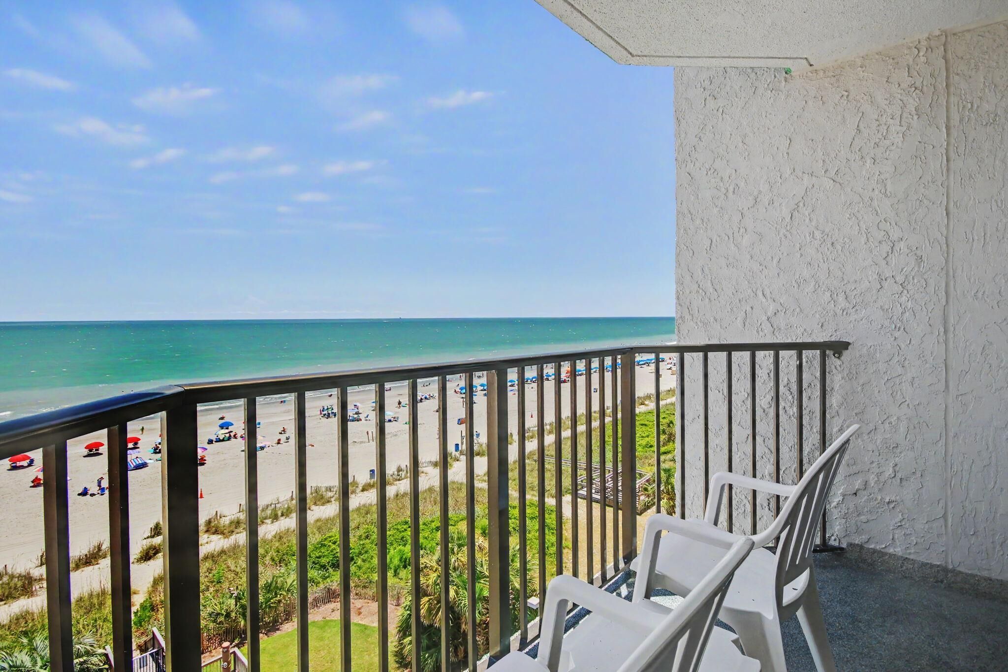 Un balcon donnant sur une plage, avec des chaises blanches et une balustrade.