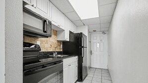 A compact kitchen with white cabinets, a black refrigerator, and a stainless steel range. - Oceanfront King Room + Beach Access + Dog Friendly (Myrtle Beach)