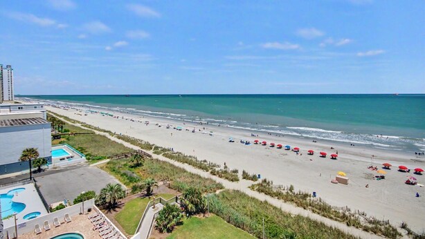A beach with a clear view of the ocean, a pool, and a building with a balcony overlooking the beach. - Oceanfront King Room + Beach Access + Dog Friendly (Myrtle Beach)