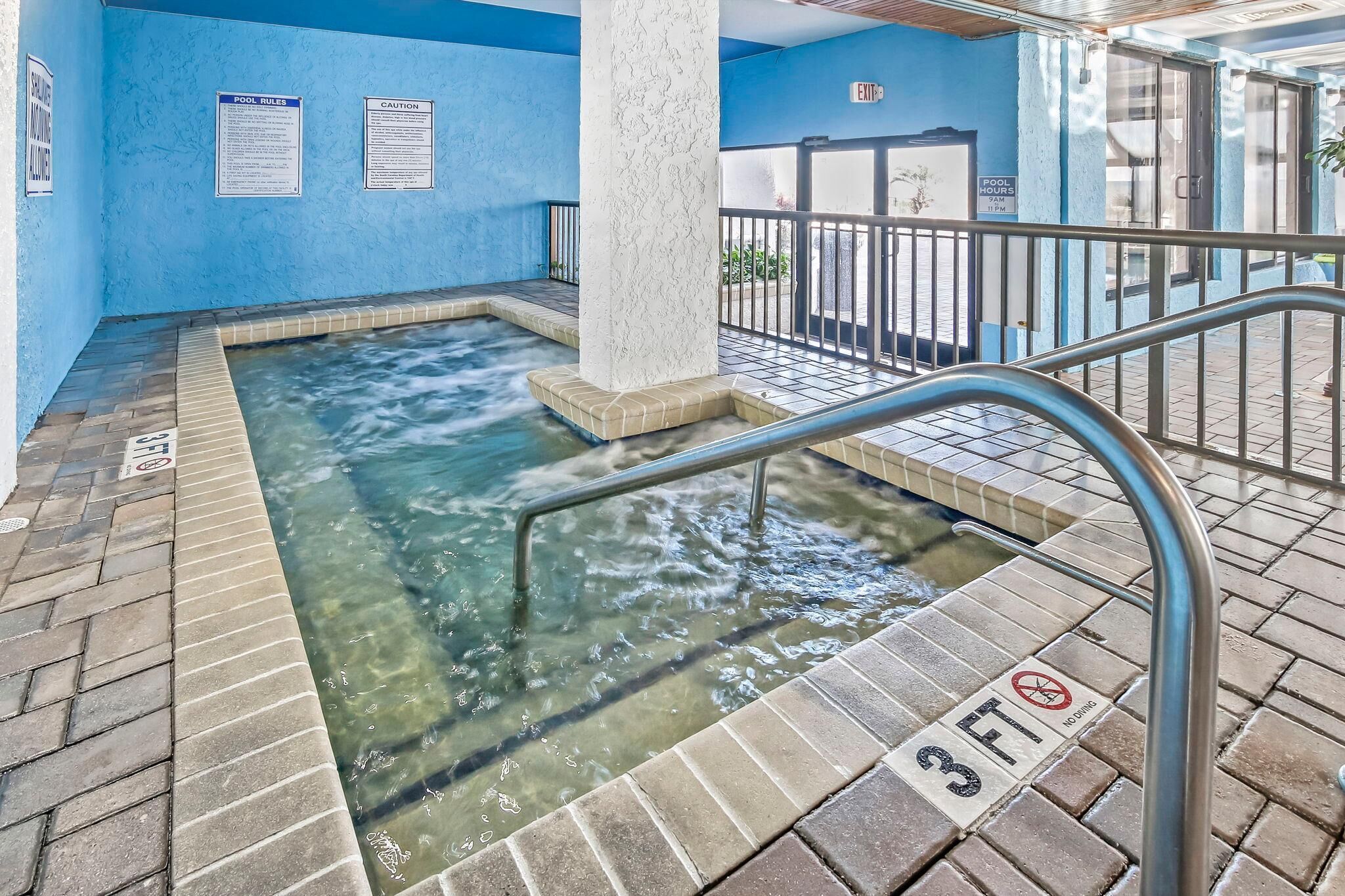Un espace piscine avec une eau claire, un panneau indiquant une profondeur minimale de 3 pieds (environ 90 cm) et interdisant les plongeons, ainsi qu’une rambarde en métal.