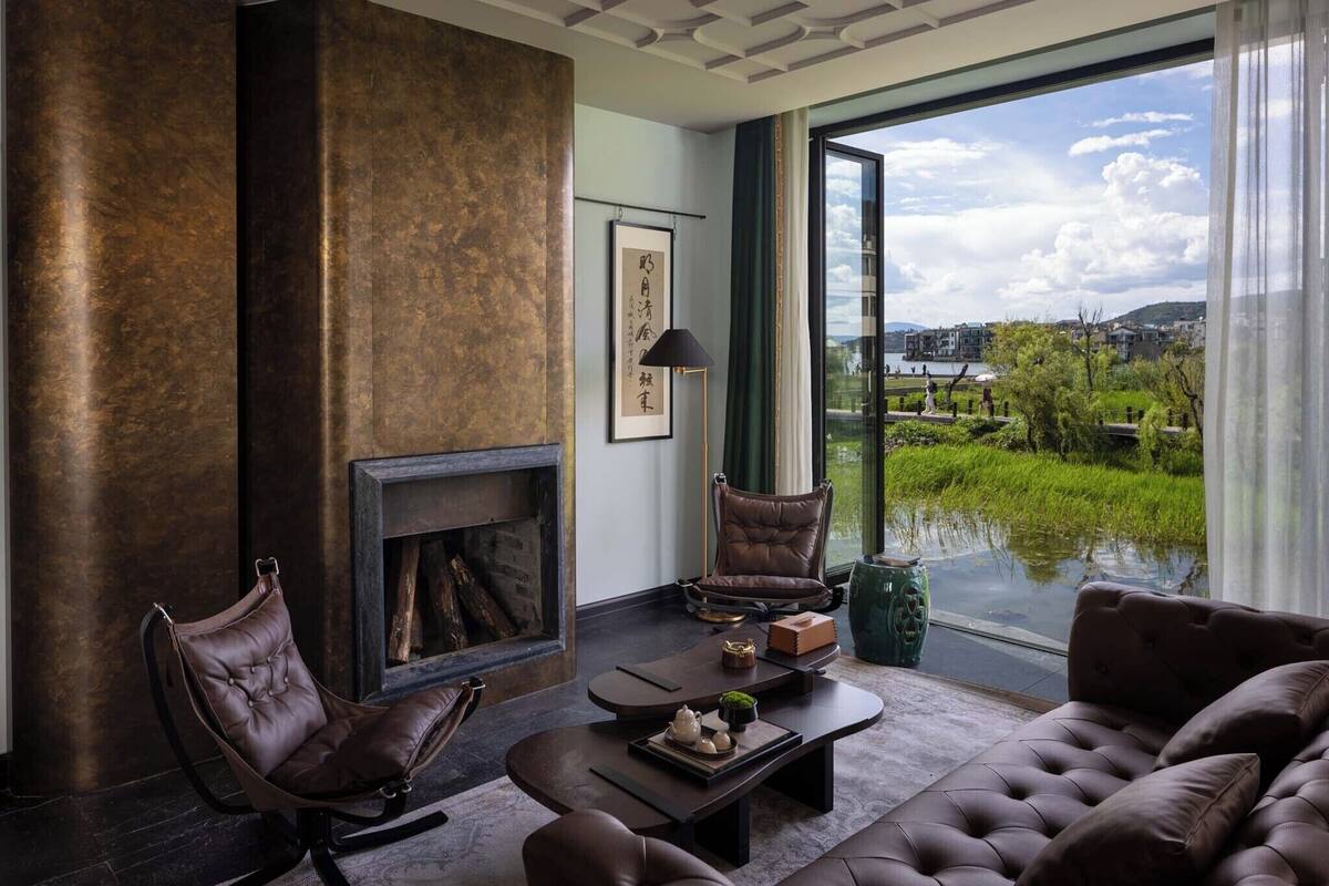 Uma sala de estar moderna com lareira, mobiliário de couro e uma ampla janela com vista para uma paisagem verde.