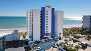 A hotel with a pool, parking lot, and a view of the beach. - Oceanfront King Room + Beach Access + Dog Friendly (Myrtle Beach)