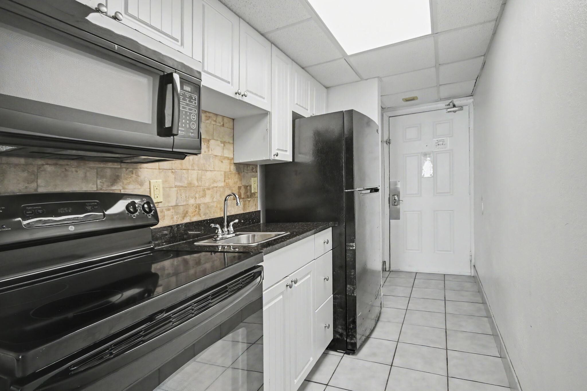 A kitchen with white cabinets, a black refrigerator, a microwave, and a stove.