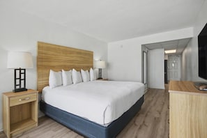 Une chambre d’hôtel moderne avec un grand lit, une tête de lit en bois, des lampes de chevet, une table de chevet en bois et un téléviseur posé sur une commode en bois.