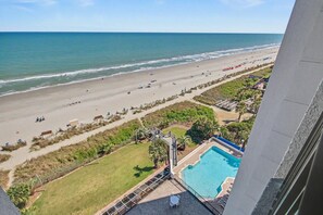 Vista al mar desde un balcón, piscina y zona verde con una escalera hacia una terraza.