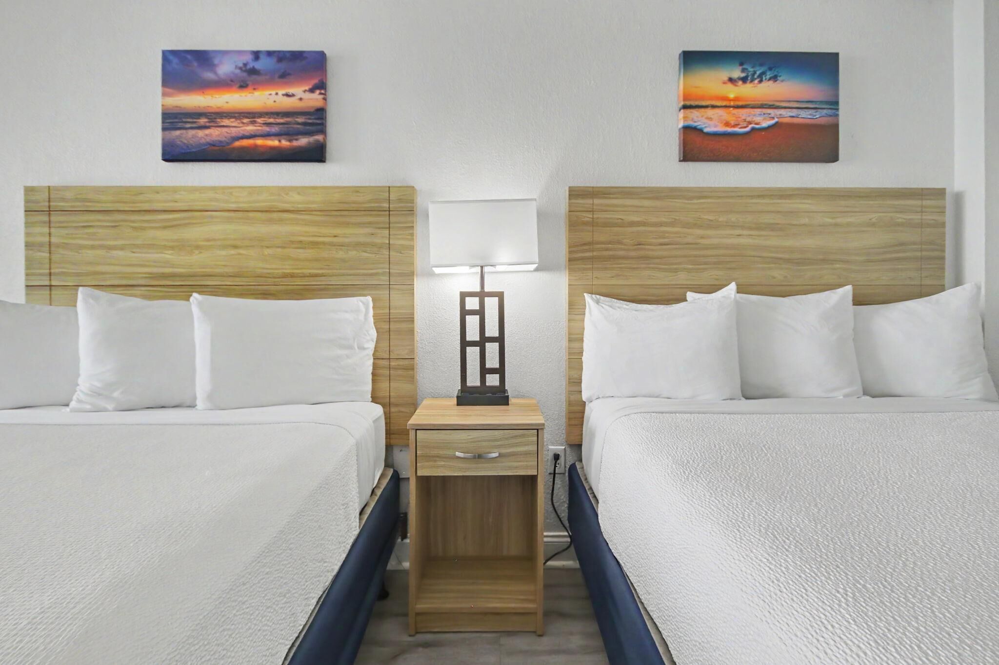 Een hotelkamer met twee bedden, een nachtkastje met een lamp en twee schilderijen aan de muur.