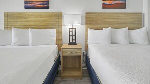 Et hotelværelse med to senge, et natbord med en lampe og to billeder på væggen.