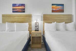 Una camera d'albergo con due letti, un comodino con una lampada e due quadri alle pareti.