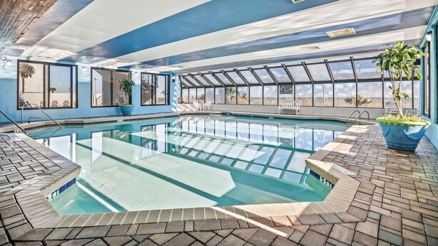 Una piscina interior con paredes de vidrio transparente, suelo de baldosas y techo azul.