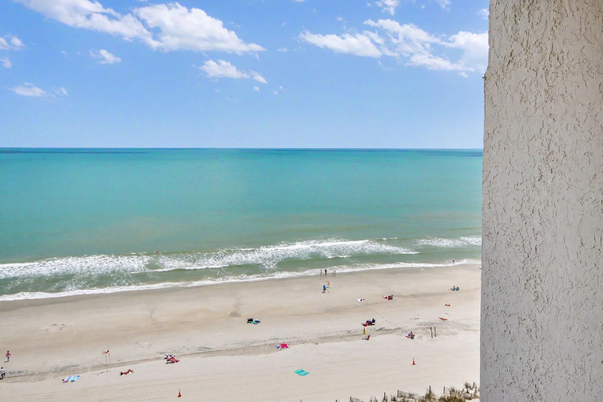 Ein Strand mit blauem Himmel, ruhiger See und Menschen, die am Ufer entlanggehen.