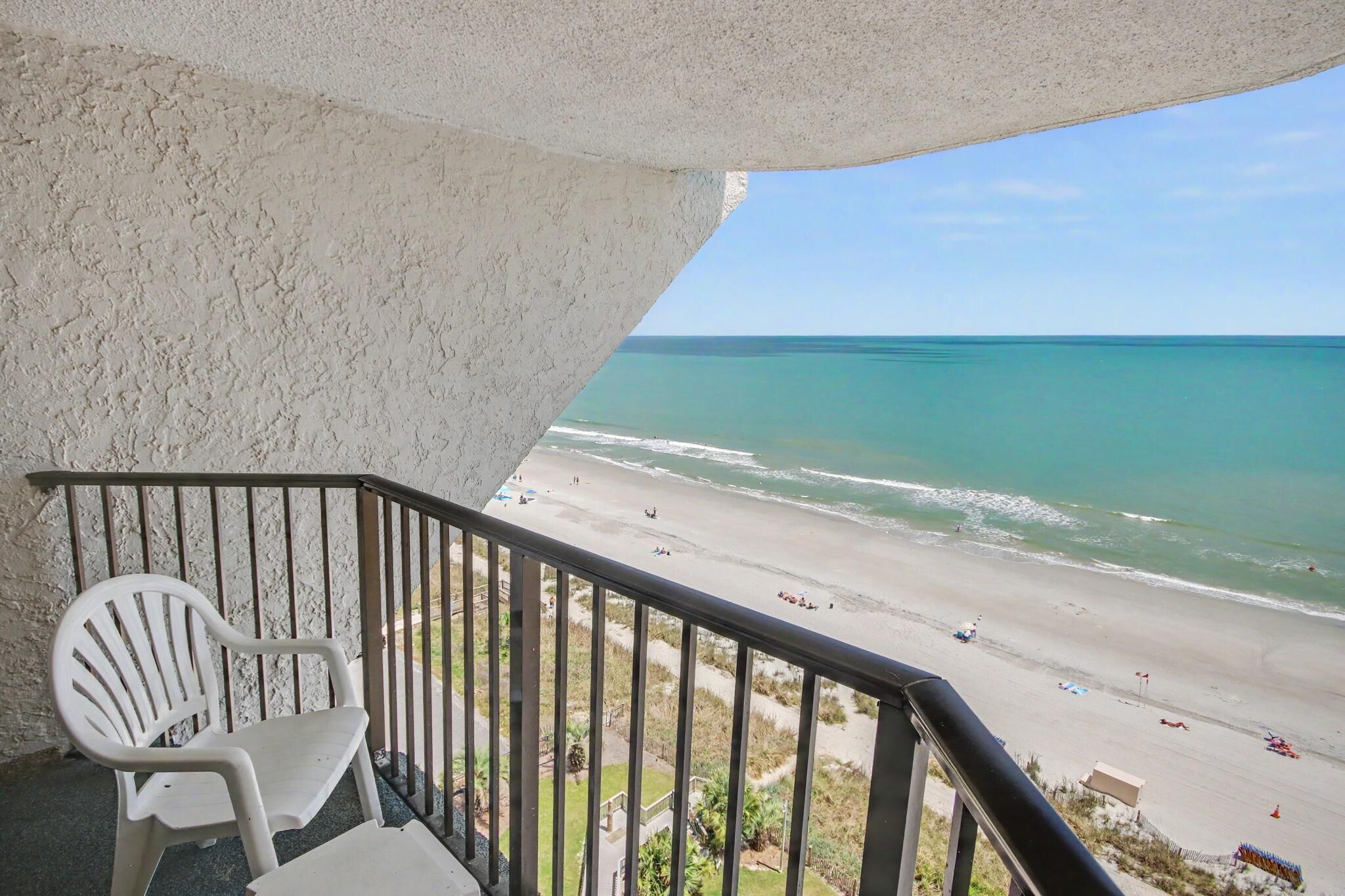 Un balcon donnant sur une plage, une chaise en plastique blanche et une rambarde.
