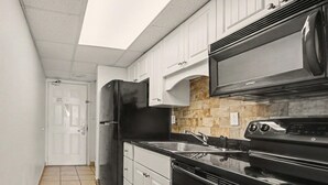A kitchen with white cabinets, a black refrigerator, a microwave, and a stove. - Oceanfront Two Queen Room + Beach + Dog Friendly (Myrtle Beach)
