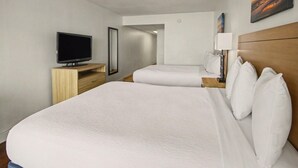 A hotel room with a large bed, a television, a bedside table with a lamp, and a painting on the wall. - Oceanfront Two Queen Room + Beach + Dog Friendly (Myrtle Beach)