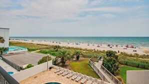 Une vue sur la plage depuis un balcon, avec une piscine et des chaises longues.