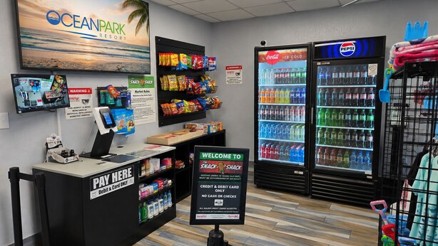 Un espace bar proposant des collations, avec un réfrigérateur Coca-Cola, des étagères remplies de snacks et un comptoir de paiement.
