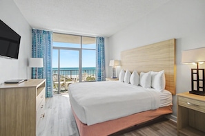 Ein Hotelzimmer mit Bett, Schreibtisch, Fernseher, einem Balkon mit Aussicht und einem Fenster mit Vorhängen.