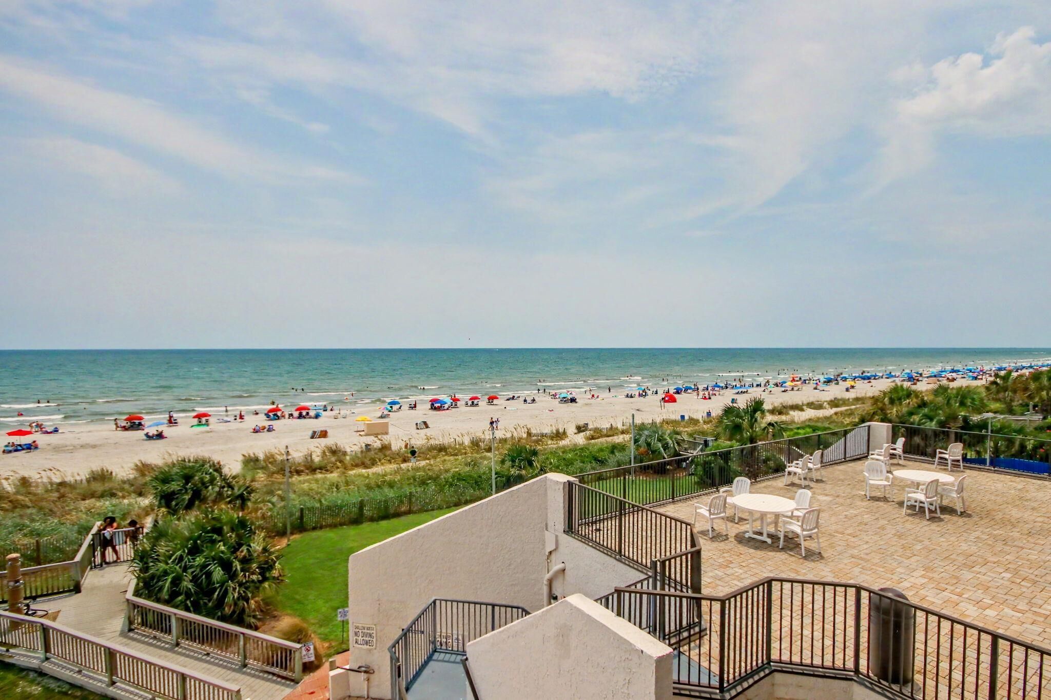 A beach with umbrellas and people, a view of the ocean, and a building with outdoor seating.