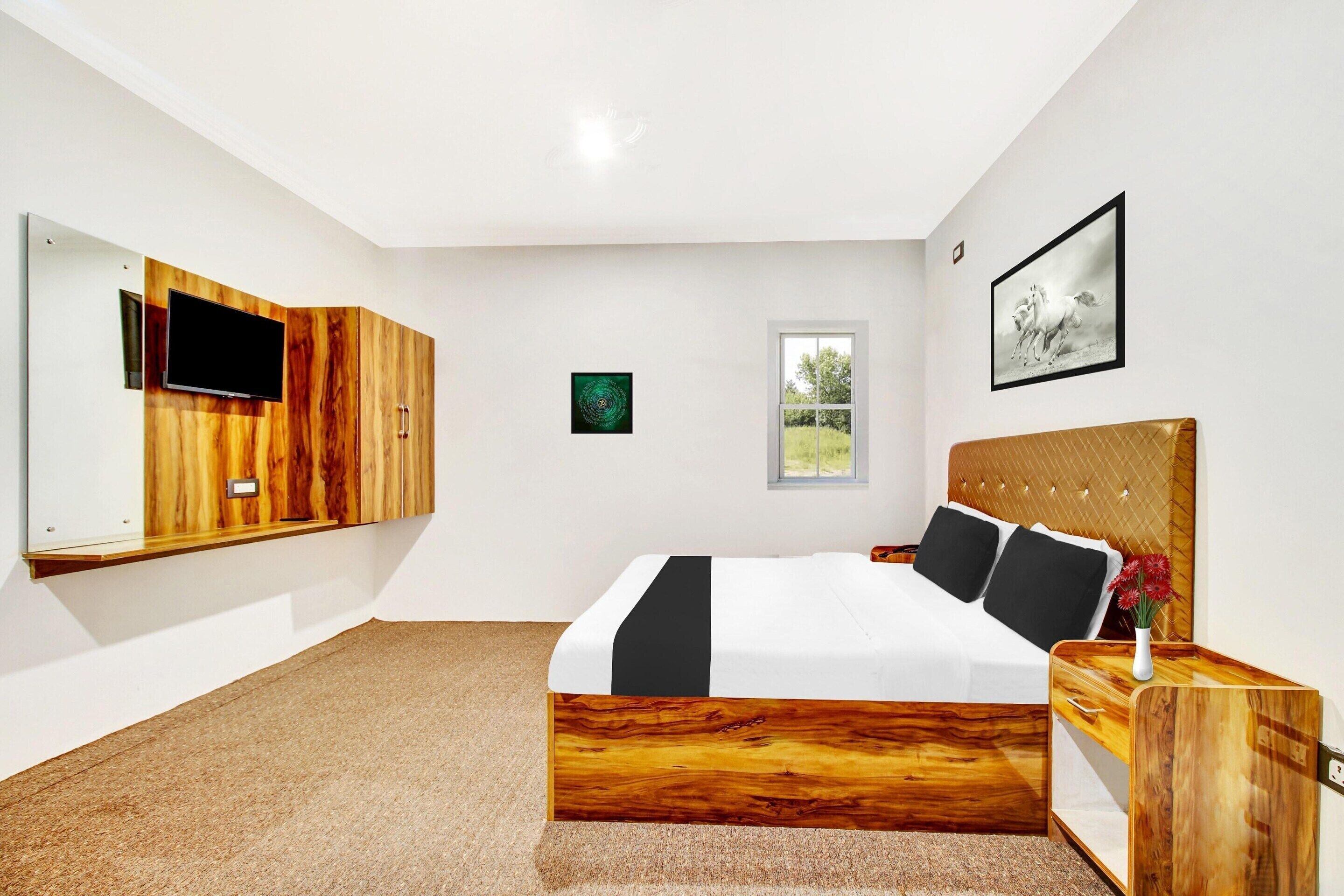 A modern bedroom with a large bed, a TV mounted on a wooden panel, a window, and a framed picture on the wall.