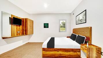 A modern bedroom with a large bed, a TV mounted on a wooden panel, a window, and a framed picture on the wall.