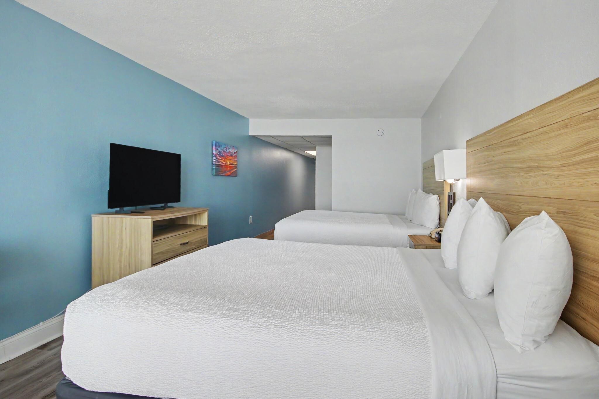 Une chambre d’hôtel avec un grand lit, un téléviseur posé sur un meuble en bois, une table de chevet avec une lampe et un mur bleu.