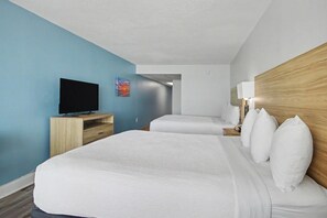 Una camera d'albergo con un letto grande, una TV su un mobile in legno, un comodino con una lampada e una parete azzurra.