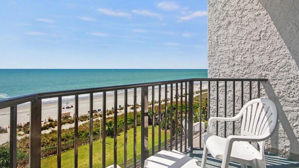 A balcony with a view of the beach, a white chair, and a textured wall. - Oceanfront Two Queen Room + Beach + Dog Friendly (Myrtle Beach)