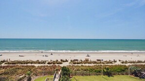 A beach with a clear sky, a sandy shore, and some vegetation in the foreground. - Oceanfront Two Queen Room + Beach + Dog Friendly (Myrtle Beach)