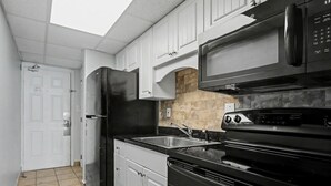 A kitchen with white cabinets, a black refrigerator, a microwave, and a stove. - Oceanfront Two Queen Room + Beach + Dog Friendly (Myrtle Beach)