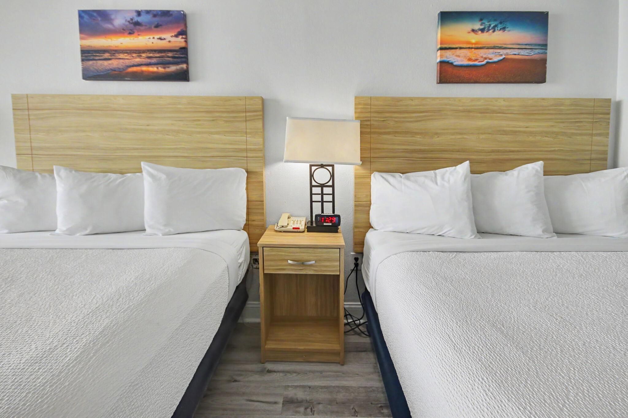 Een hotelkamer met twee bedden, een nachtkastje met een lamp, een telefoon en een wekker.