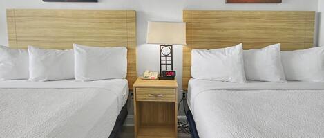 Een hotelkamer met twee bedden, een nachtkastje met een lamp, een telefoon en een wekker.
