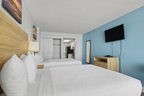 Hotellihuone, jossa on kaksi sänkyä, seinälle asennettu televisio ja näkymä keittiötilaan.