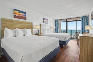 Ein Hotelzimmer mit zwei Betten, einem Schreibtisch, einem Sessel, einem Balkon mit Aussicht und Bildern an den Wänden.