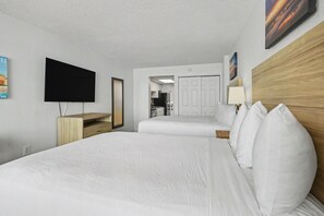Ein Hotelzimmer mit einem großen Bett, einem an der Wand montierten Fernseher, einem Holz-Kopfschild und einer Tür zu einem Küchenbereich.
