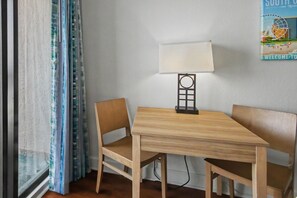 Une pièce avec une table en bois, deux chaises, une lampe et une fenêtre avec des rideaux.