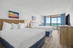 Habitación de hotel con dos camas, un escritorio, televisor y balcón con vistas.