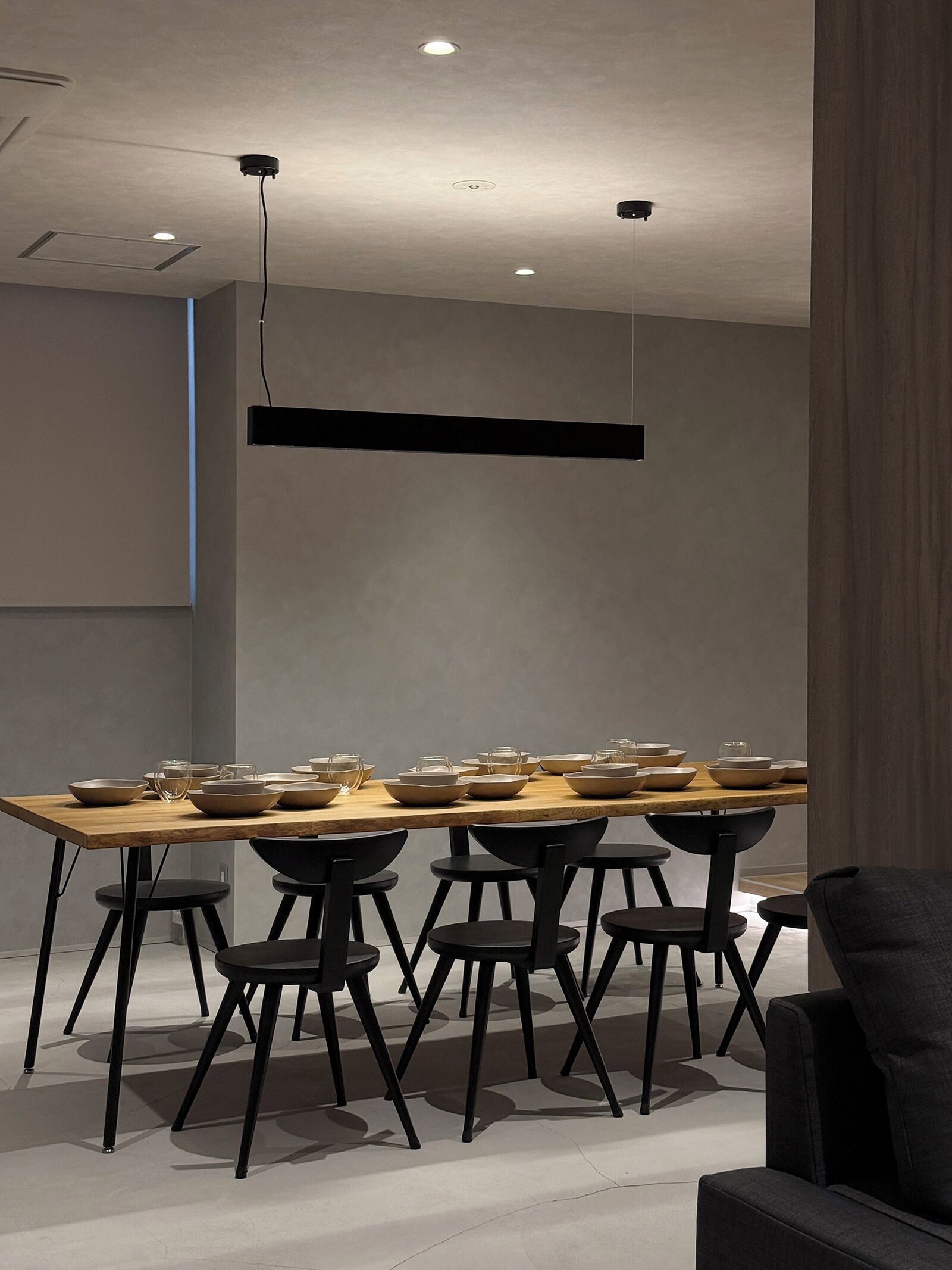 A modern dining area with a long table, black chairs, and pendant lighting.