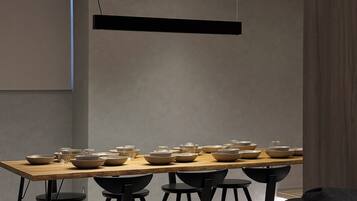 A modern dining area with a long table, black chairs, and pendant lighting.