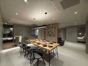 A modern dining area with a long table, black chairs, and a decorative wall panel. - WAKO Ekimae (Hiroshima City)