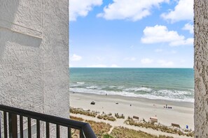 Blick auf einen Strand vom Balkon mit Geländer, feiner Sand, Meer und klarer Himmel.