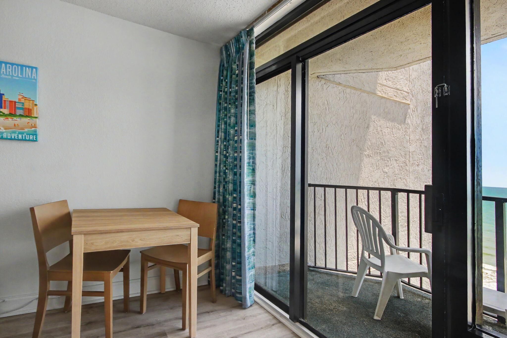 Ein Balkon mit Blick auf den Strand, ein Holztisch mit Stühlen und ein Poster an der Wand.