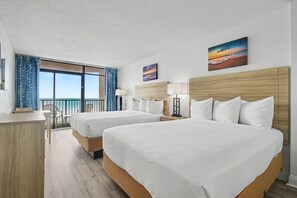Une chambre d’hôtel avec deux lits, un bureau, une chaise, un balcon avec vue et des œuvres d’art aux murs.