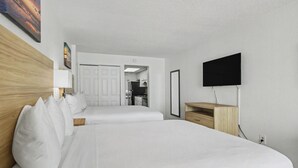 Habitación de hotel con una cama grande, un televisor montado en la pared, cabecero de madera y vista al área de la cocina.