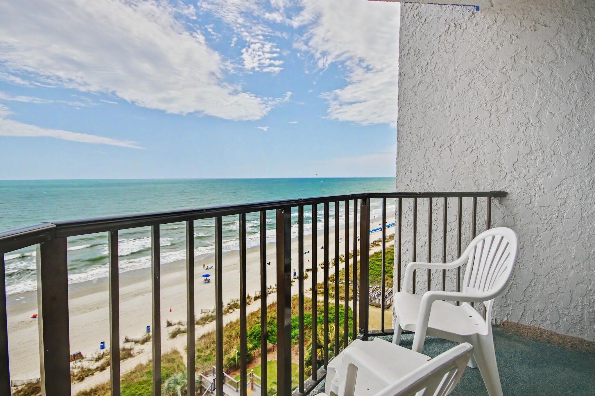 A balcony with a view of the beach and ocean, a white plastic chair, and a textured wall.