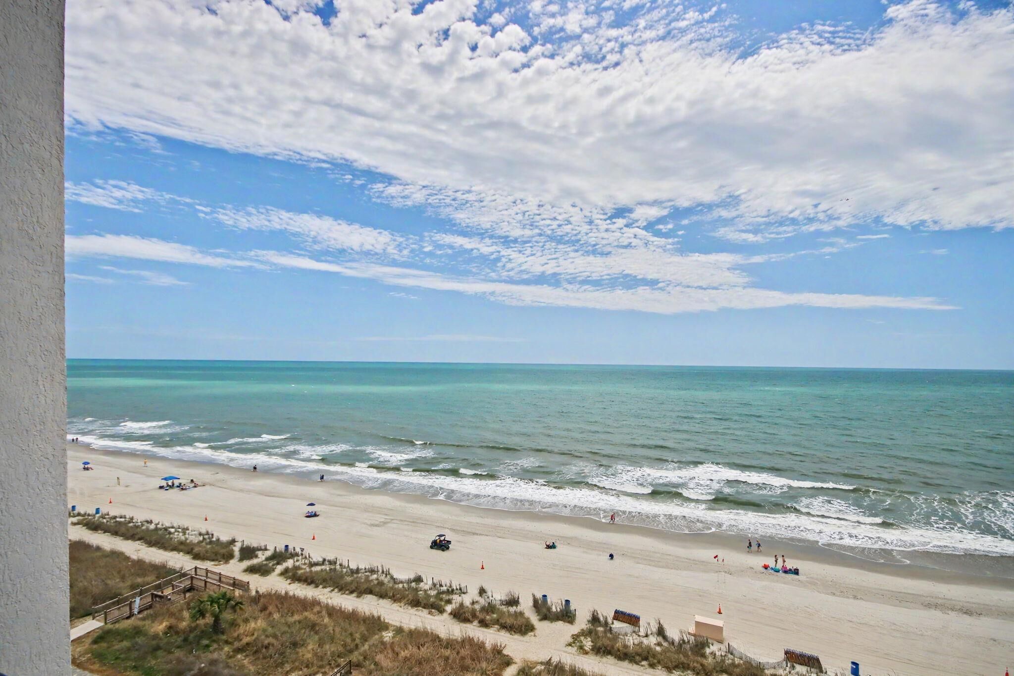 A beach with a clear sky, calm sea, and a sandy shore with people and vehicles.