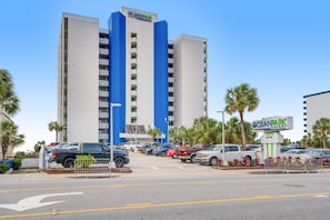 A hotel with a prominent 'OceanPark' sign, a parking lot with multiple cars, and a clear sky. - Oceanfront | Kitchen | Dog Friendly | Pools&HotTub (Myrtle Beach)