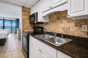 Une cuisine moderne dotée de plans de travail en granit, d’éviers en acier inoxydable et d’un four à micro-ondes.