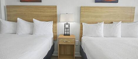 Une chambre d’hôtel avec deux lits, une table de chevet avec une lampe et deux tableaux représentant un coucher de soleil accrochés au mur.