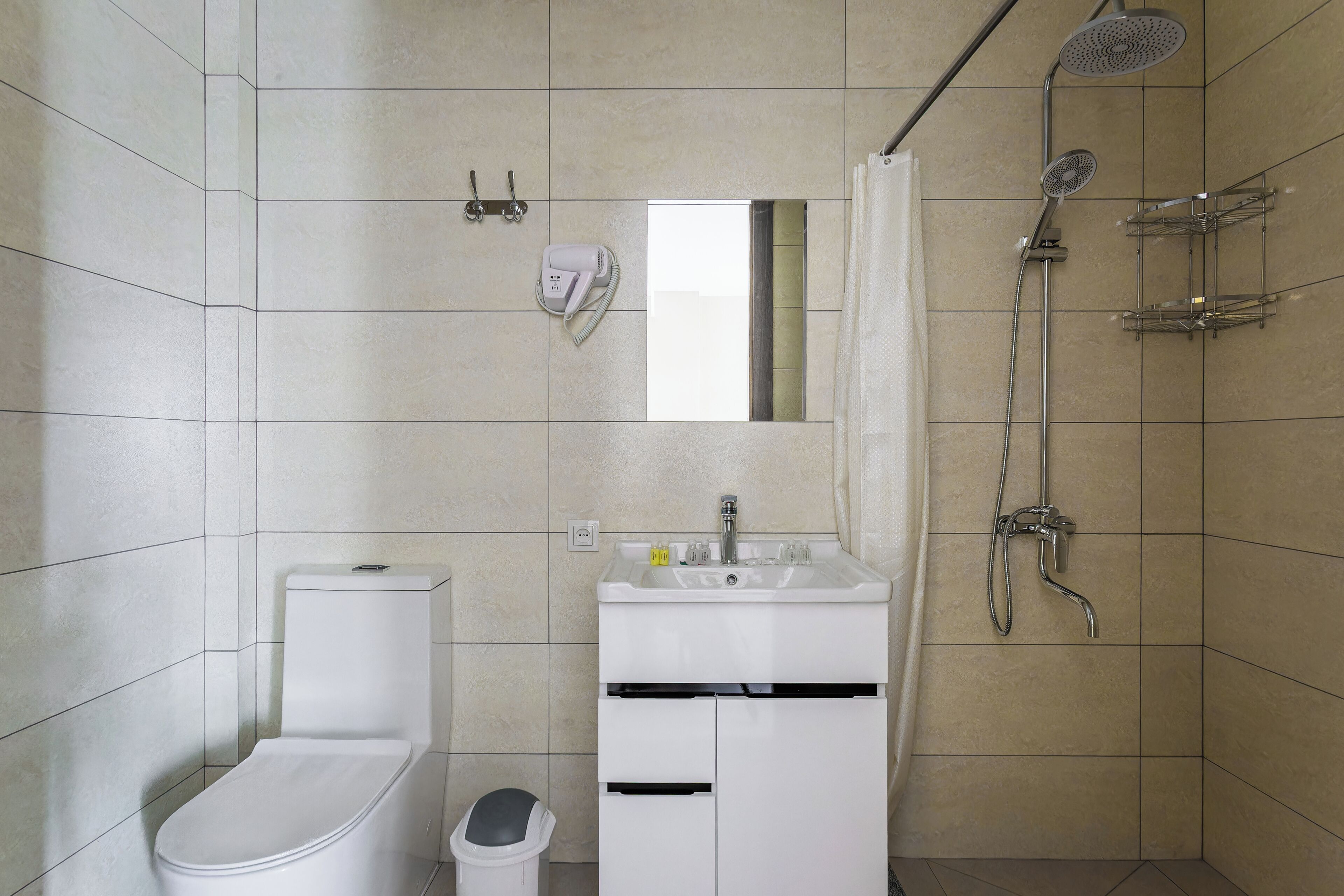 Een badkamer met toilet, wastafel, spiegel, douche en prullenbak.