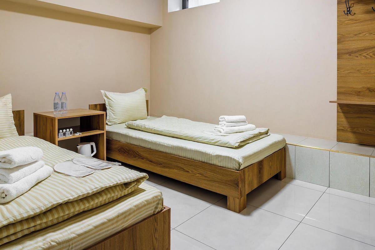 A hotel room with two beds, a wooden shelf with toiletries, and a wooden wall panel.