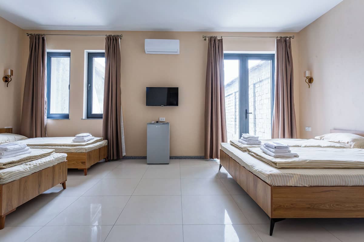 A hotel room with two beds, a TV, an air conditioner, and a window with curtains.